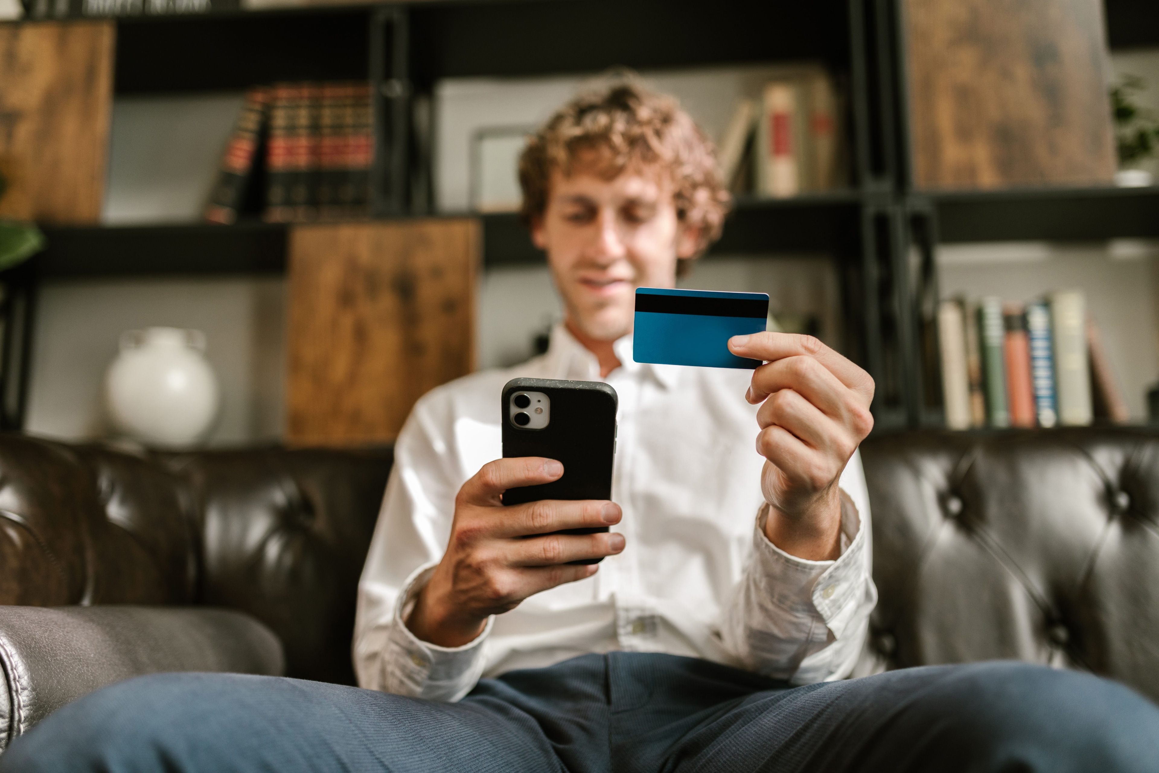 Man on a leather couch holding a smartphone and a bank card